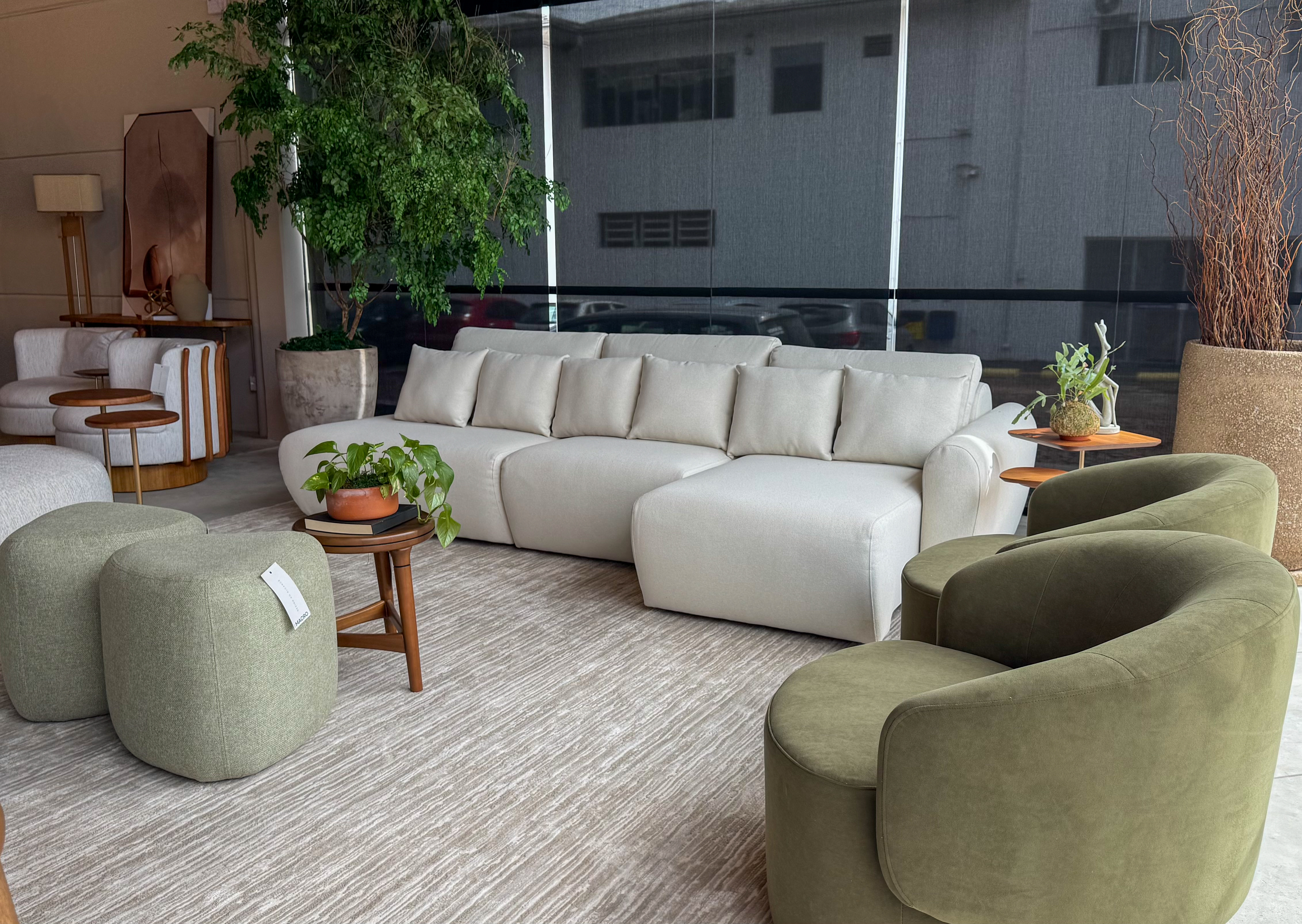 Sofá off-white com poltronas giratórias verdes e pufes no showroom Macro Ambientes.