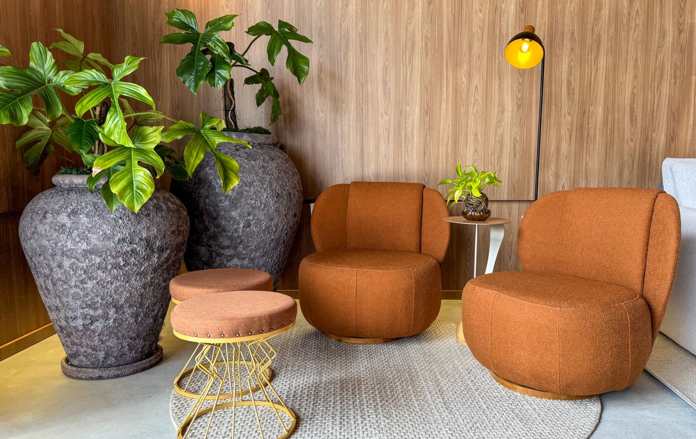 Poltronas giratórias terracota, banquinho dourado e vasos de plantas no showroom Macro Ambientes.