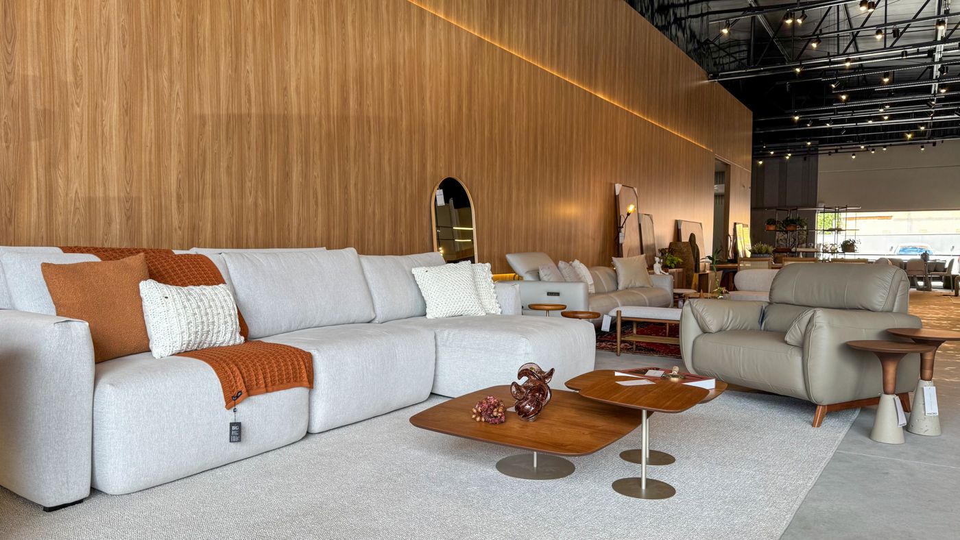 Showroom Macro Ambientes com sofá modular claro, mesas de centro em madeira e painel amadeirado.